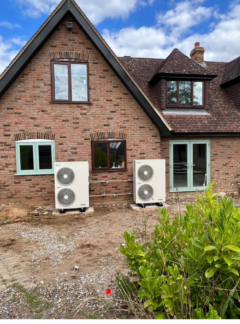 Two twin-fan air source heat pumps installed side by side on level bases against a brick gable elevation