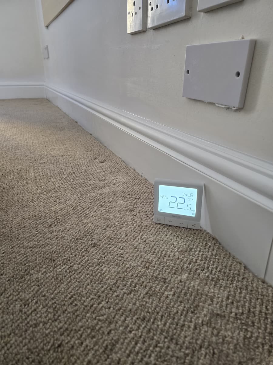 Room thermostat reading 22.5 degrees beside ThermaSkirt on a carpeted floor